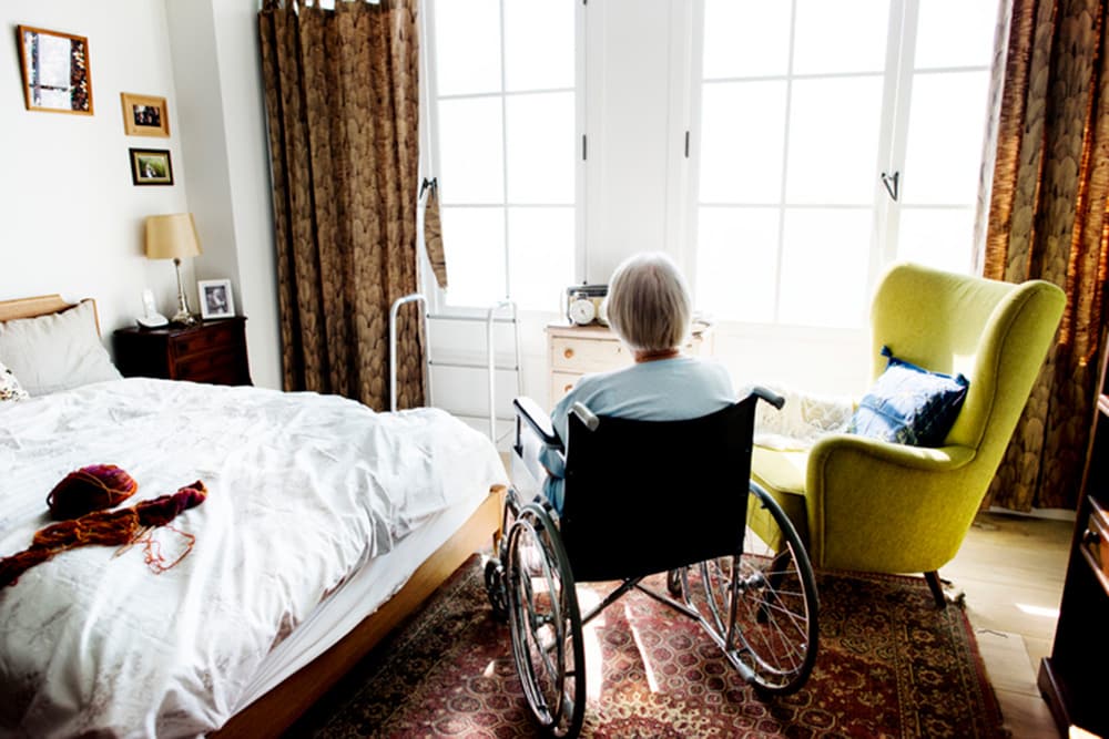Elderly Woman in Wheelchair in Bedroom Looking Out Window